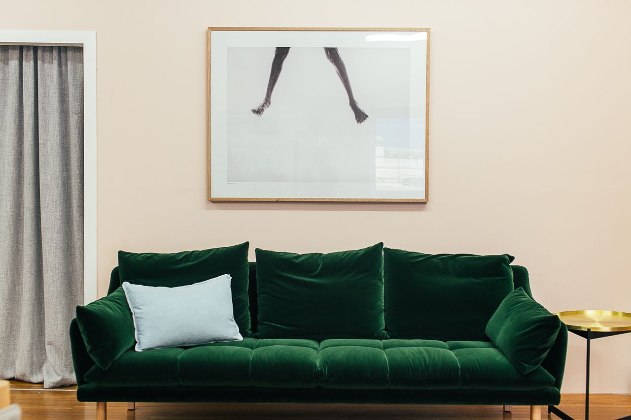 services-04 Comfortable green velour sofa with soft cushions and small round table placed on parquet floor near wall with creative framed picture in stylish living room